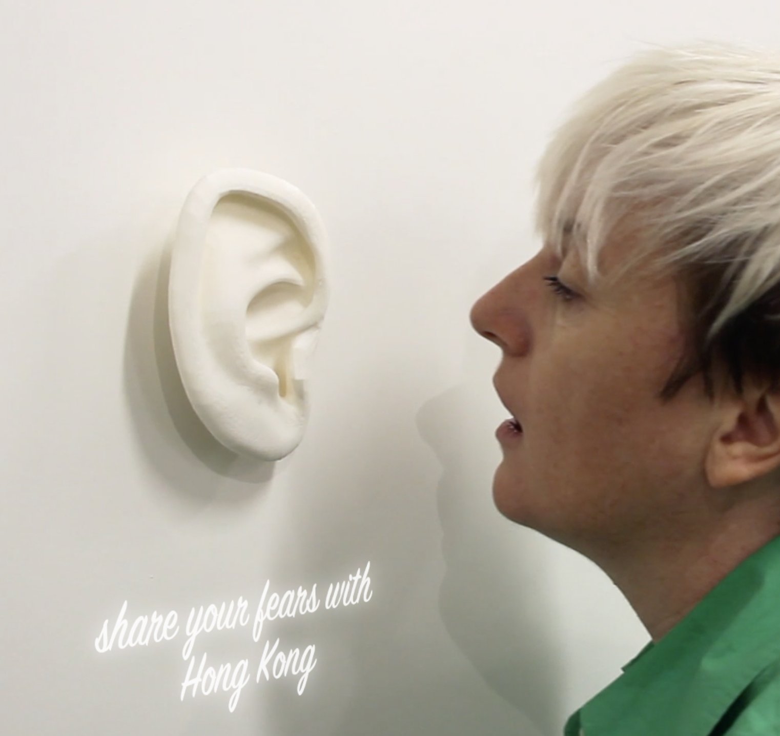 Fear Exchange: woman whispering into a sculptural ear on a wall