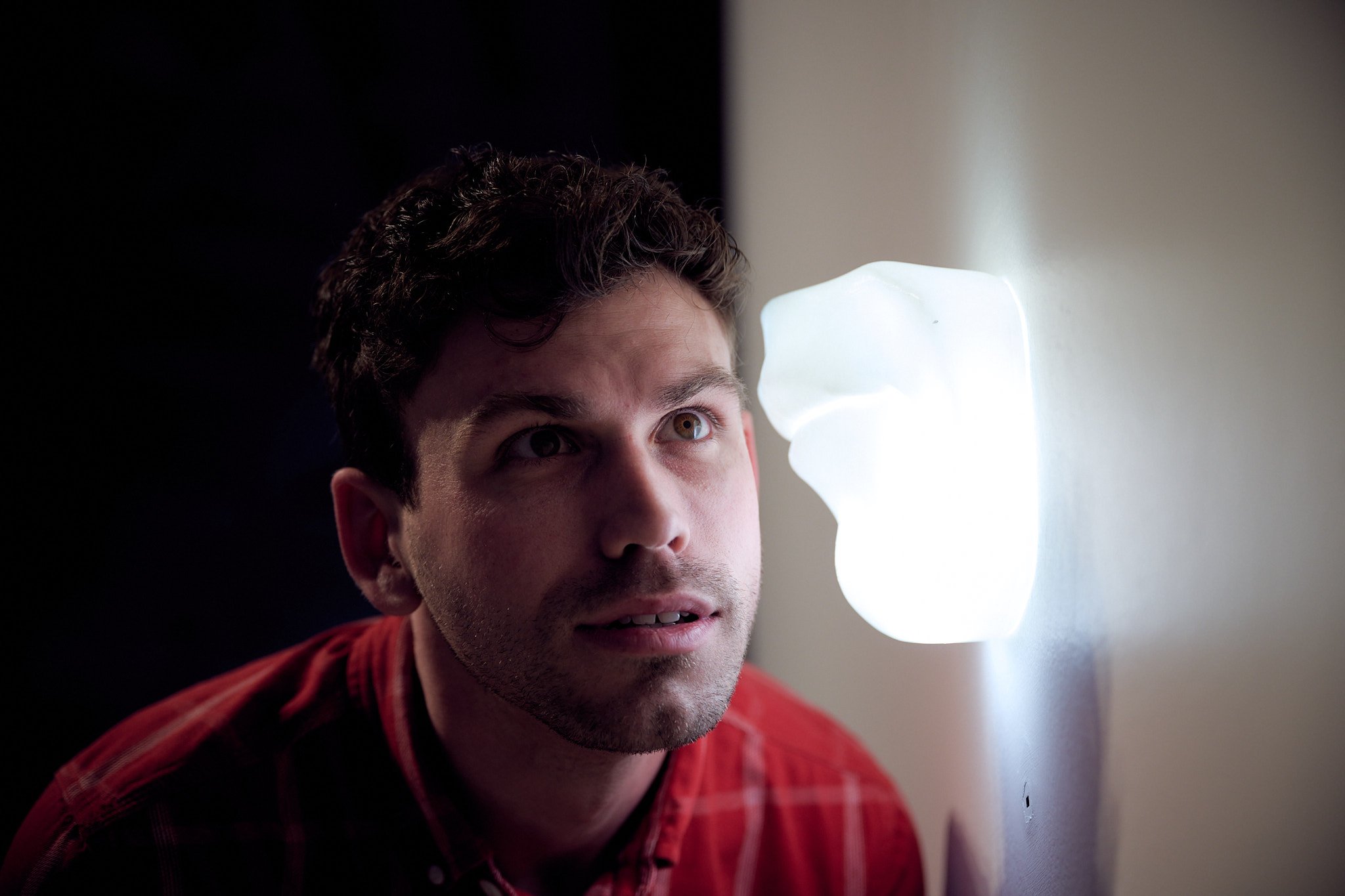 Participant leaning towards a glowing sculptural ear on the wall, Fear Exchange
