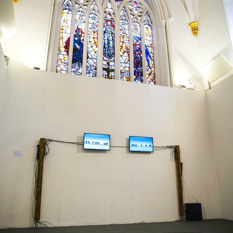 Birds on a Wire installed in a chapel, beneath stained-glass windows