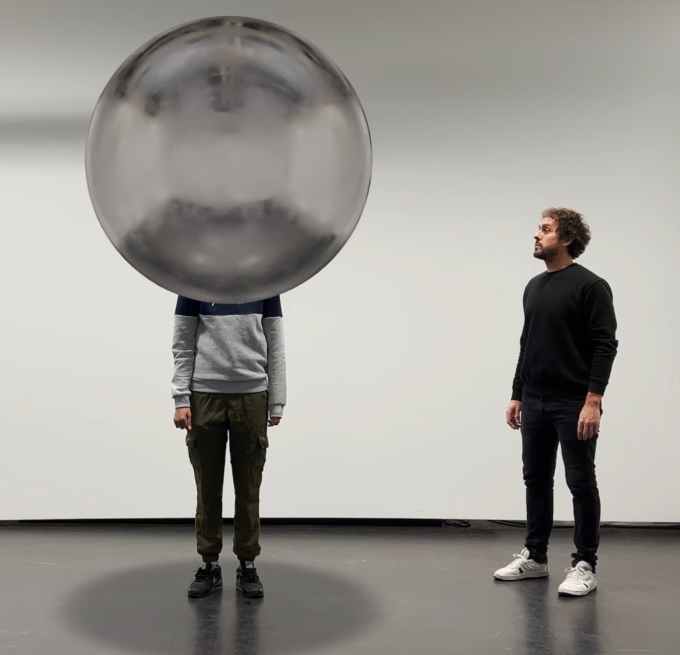 Algorithmic Amplification: a person whose head is hidden by a reflective sphere, next to an observer